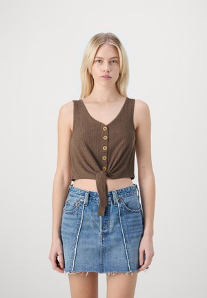 Brun ribbet crop top med V-udskæring og frontknude, med træknapper. Sættes sammen med en blå denim mini-skjorte med rå kant.