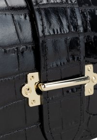 Primo piano di una borsa in pelle nera lucida con texture a coccodrillo, dotata di una chiusura in metallo dorato e dettagli di cucitura.