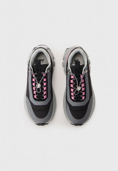 Athletic sneakers with a black and gray upper, pink laces, and a bulky sole. Features metallic hardware and textured fabric accents.