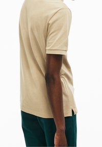 Polo de manga corta beige hecho de algodón texturizado, con un dobladillo recto y aberturas laterales, combinado con pantalones verde oscuro.
