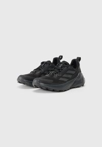 Des chaussures de sport noires avec une tige en mesh, une semelle en caoutchouc texturé, un bout renforcé et deux languettes pour un enfilage facile.