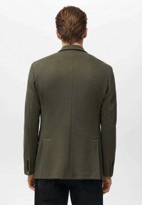 Oliven grøn blazer med en struktureret finish, enkeltspændt design, indsnævrede revers og to forlommer. Glat ryg med knapmanchetter.
