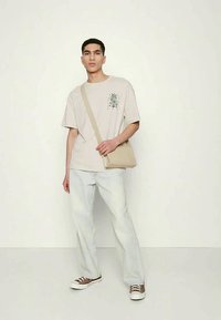Beige graphic t-shirt, relaxed fit, paired with light wash jeans and brown sneakers. Accessorized with a tan crossbody bag.