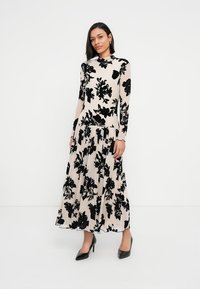 Μάξι φόρεμα από διάφανο μπεζ ύφασμα, με μαύρο λουλουδάτο σχέδιο. Μακριά μανίκια, εφαρμοστό μπούστο, πλισέ φούστα, συνδυασμένο με μαύρες γόβες.