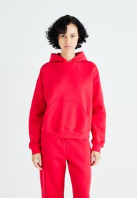 Hanorac roșu dintr-un material moale, având un buzunar frontal și glugă cu șnur; asortat cu pantaloni roșii pentru un look coordonat.