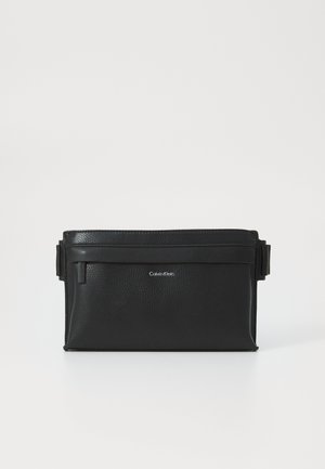 Juodas odinis krepšys su tekstūruota paviršiumi, stačiakampio formos, viršuje užtrauktuku uždaromas ir su reguliuojama petneša. Pabrėžia Calvin Klein logotipas.