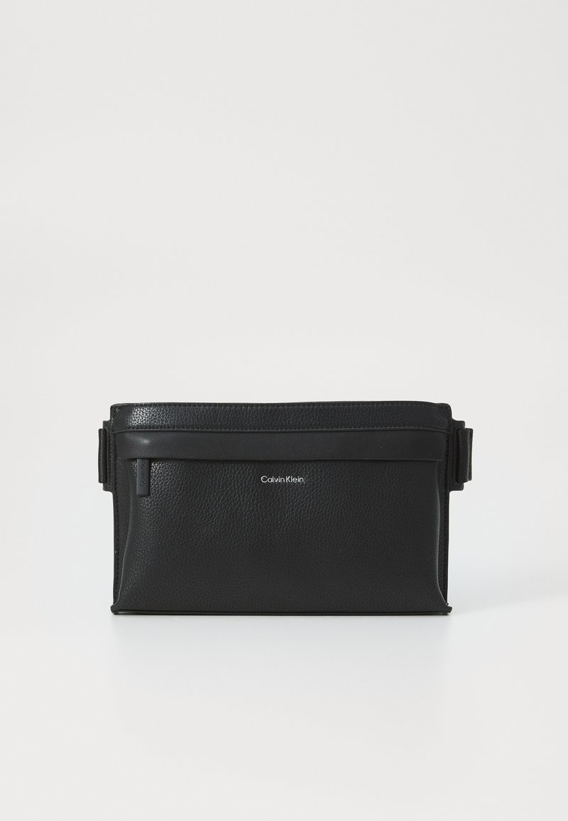 Black leather bag with textured surface, rectangular shape, top zipper closure, and an adjustable strap. Features Calvin Klein logo.