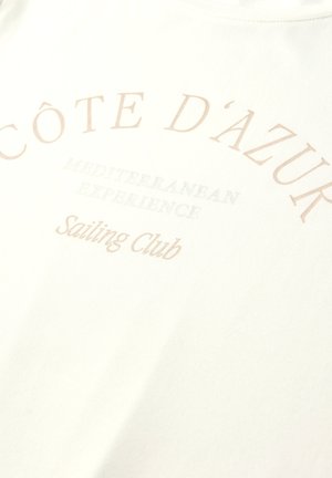 Côte d'Azur Sejlklub tekst i lys beige på hvidt stof med "Mediterranean Experience" i mindre, falmet skrift nedenunder.