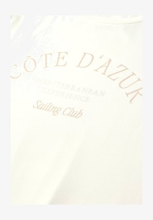 Côte d'Azur Sejlklub tekst i lys beige på hvidt stof med "Mediterranean Experience" i mindre, falmet skrift nedenunder.