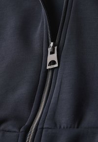 Marinblå zip-jacka med en slät tygtextur, metallisk dragkedja och sömmar längs dragkedjan.