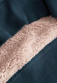 Combinație de material formată dintr-un material ribbed bleumarin deasupra unei texturi pufoase, de un roz deschis și moale. Detalii ale cusăturilor vizibile de-a lungul marginilor.