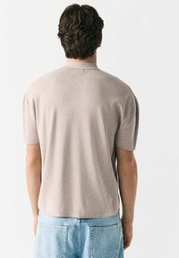 Kortærmet, beige strikket polo med en tekstureret overflade og diskrete kravedetaljer, parret med lyseblå denimshorts.