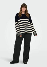 Gestreepte gebreide trui in marineblauw en roomkleur, met brede mouwen met gestreepte accenten. Gecombineerd met zwarte breedpijperige broeken en zwarte schoenen.