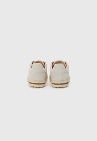 Beige ruskinn sneakers med rund tå og myk tekstur, med en lysfarget gummisåle og minimal merking på baksiden.