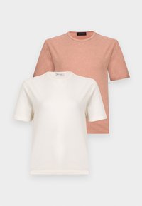 Δύο μονόχρωμες μπλούζες με στρογγυλή λαιμόκοψη, μια μπεζ μπροστά και μια σκονιστή ροζ πίσω, τοποθετημένες σε ανοιχτό γκρι φόντο.