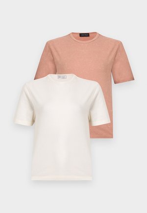 Femme portant un haut beige à manches courtes, un jean large foncé, des talons beiges, des boucles d'oreilles anneaux dorés et des lunettes de soleil marron, debout avec une main sur la hanche.