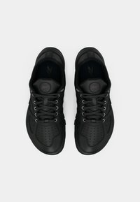 Sapatos atleticos pretos com um design perfurado, atacadores redondos e uma língua almofadada. O material parece sintético, com uma sola plana.