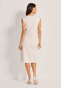 Knielanges, ärmelloses Kleid in hellem Creme mit strukturierter Blumenmusterung. Verfügt über einen runden Ausschnitt und eine gerade Passform. Getragen mit hochhackigen Sandalen.