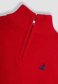 Rode gebreide trui met een hoge geribbelde kraag, voorzien van een halflange rits aan de voorkant en een klein blauw zeilbootlogo op de borst. Soepele textuur.
