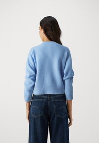 Jasnoniebieski prążkowany sweter z długimi rękawami, okrągłym dekoltem i krótkim krojem, zestawiony z ciemnymi dżinsami z wysokim stanem.