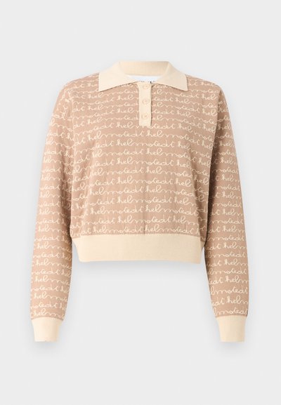 Gaiša adīta jakas ar polo apkakli, kurā ir atkārtoti balti roku rakstīti teksti. Saīsināts dizains ar ribotām piedurknēm un apakšmalu.