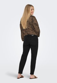 Jean noir slim, porté avec un blouse à motifs léopard marron. La tenue présente un design décontracté et une coupe relax, complétée par des sandales.