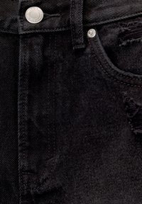 Musta farkkushortsit, joissa on kulunut tasku, metallinappi ja näkyvät ompelupatternit, esittelevät tekstuurista kangaspintaa.