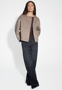 Bruine wollen jas met een minimalistisch design, voorzien van een ronde halslijn en voortassen, gecombineerd met donkere denim wijde broek.