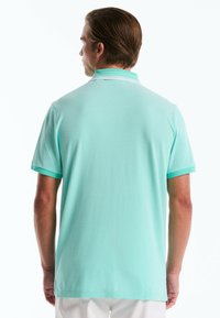 Polo mint vert avec manches courtes, un col avec deux rayures blanches, et un tissu texturé. La vue arrière montre une coupe droite et des fentes sur les côtés.