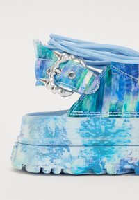 Sandales plateformes bleues avec une tige en tissu texturé affichant un design abstrait, dotées d'une boucle métallique et d'accents de lacets assortis.