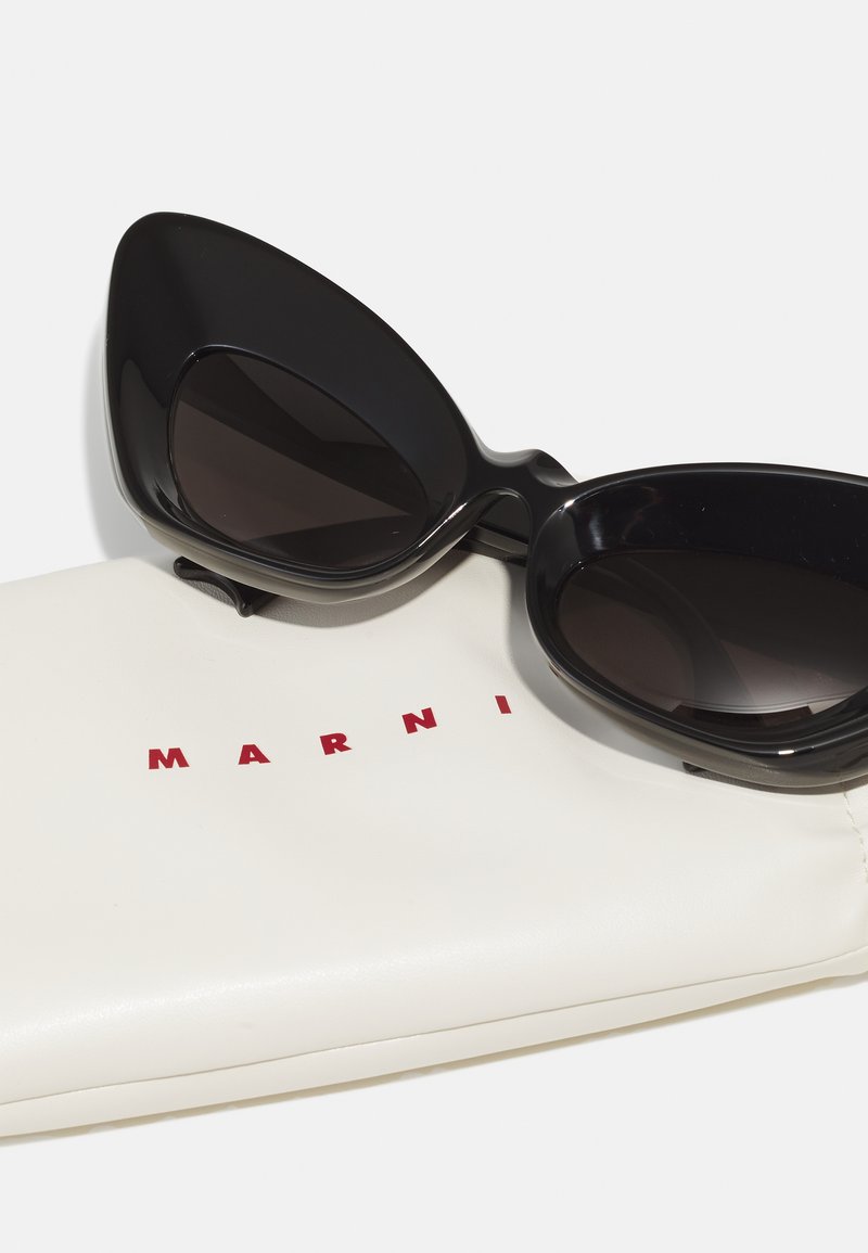 Black cat-eye sunglasses with dark lenses resting on a white soft case. The case features a red "MARNI" logo.