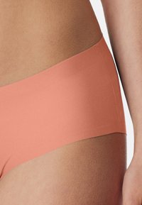 Peach-colored seamless hipster underwear made of smooth fabric, featuring a low-rise design and soft elastic waistband.