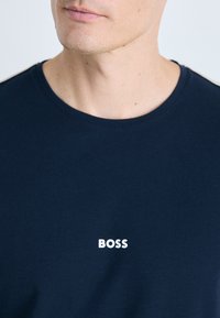 Marineblå bomull T-skjorte med klassisk rund hals, med en hvit "BOSS" logo på brystet. Myk tekstur, minimalistisk design.