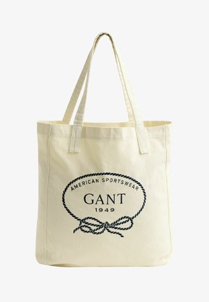 Beige canvas totebag met dubbele handgrepen, met de tekst "American Sportswear GANT 1949" en een koordontwerp in zwart op de voorkant.