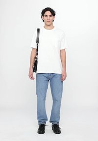 Baltas kokvilnas T-krekls ar krūšu kabatu, kombinēts ar gaiši zilām taisnajām biksēm un melniem kurpēm ar auklēm. Modelis nēsā melnu plecu somu.