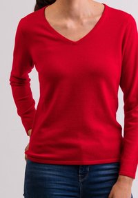 Maglione rosso lavorato a maglia con scollo a V, maniche lunghe e trama liscia, abbinato a jeans blu, con un design aderente.