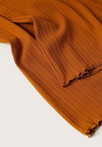 Tissu texturé et extensible dans une teinte orange brûlé chaude, avec des rayures verticales et un détail d'ourlet brut non fini.