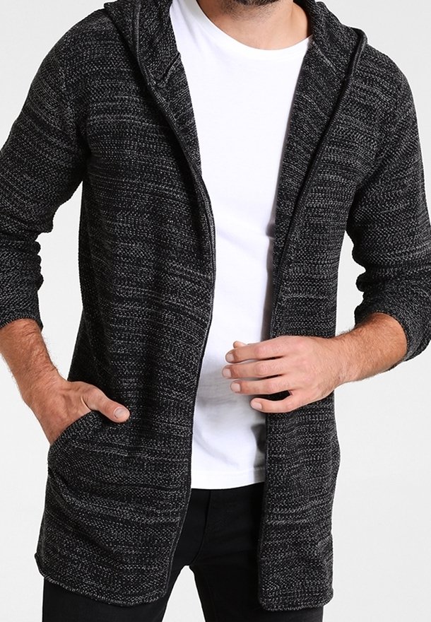 Cardigan con cappuccio in un tessuto lavorato in nero e grigio. Presenta una cerniera, maniche lunghe e due tasche frontali. Indossato sopra una t-shirt bianca.