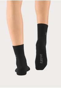 Black ribbed socks with a short cuff, featuring a logo printed on the side. Material appears soft and breathable with a smooth texture.