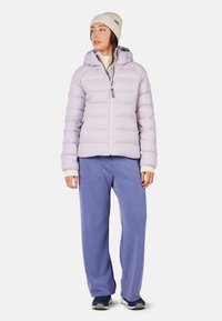 Lyse lilla pufferjakke med hætte, frontlynlås og sidelommer, parret med løse blå sweatpants og en cremet strikket hue.