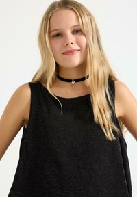 Czarny top bez rękawów o luźnym kroju, z delikatną teksturą brokatu. W zestawie aksamitny choker z zawieszką w kształcie serca.