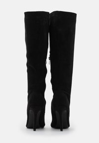 Botas altas hasta la rodilla de ante negro con un diseño elegante, punta afilada y tacón de aguja. Cuentan con una cremallera lateral para facilitar su uso.