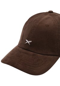 Cappellino da baseball in corduroy marrone con visiera curva, caratterizzato da un piccolo logo ricamato in bianco sul davanti. Tessuto testurizzato e design strutturato.