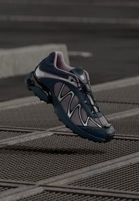 Zapatilla deportiva en azul marino y rosa con parte superior de malla, acentos reflectantes y suela flexible. Cuenta con un sistema de cordones rápido y un patrón de agarre prominente.