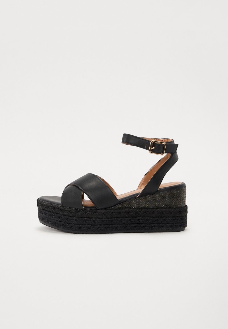 Sandales à talons compensés en cuir noir avec des brides croisées, une bride de cheville avec boucle et une plateforme en espadrille tissée noire texturée.