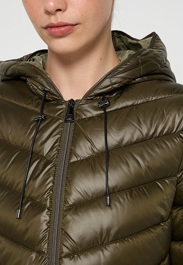 Chaqueta acolchada verde oliva con capucha, presenta un cierre con cremallera en la parte frontal, un patrón acolchado y cordones negros en el cuello para un ajuste ajustable.