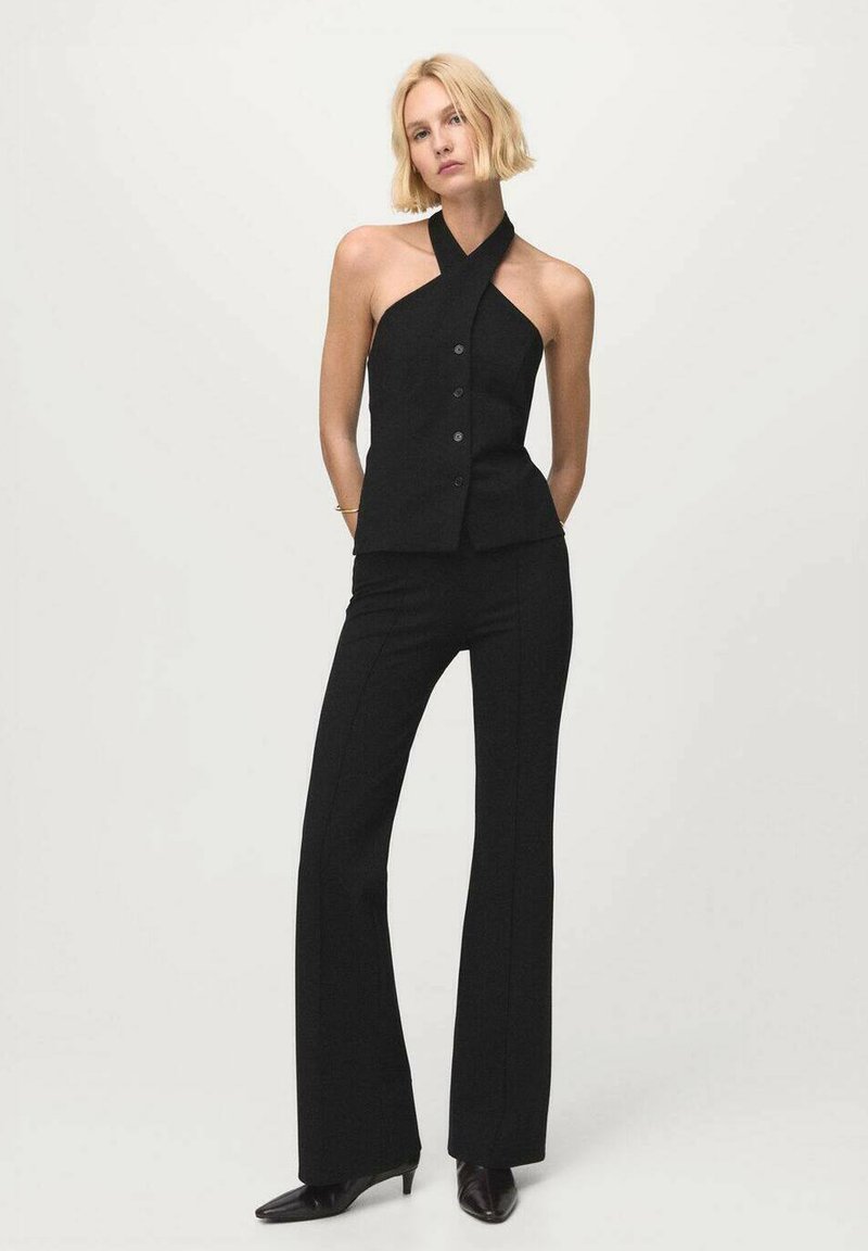 Čierny prispôsobený halter top s prekríženým výstrihom a zapínaním na gombíky, doplnený o zodpovedajúce vysoké rozšírené nohavice a čierne špicaté podpätky.