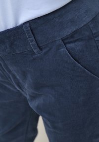 Marine corduroy broeken met een gestructureerd ribbeloppervlak, voorzien van een platte tailleband en zijzakken, waarbij een close-up van de stof en het ontwerp wordt vastgelegd.