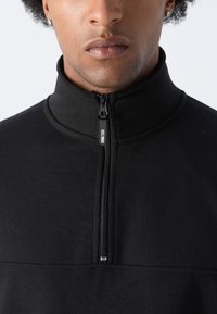 Black quarter-zip pullover made of soft fabric with a smooth texture, featuring a stand-up collar and a silver zipper detail.