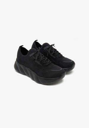 Zwarte sneakers van een textiele stof met gladde accenten, voorzien van een chunky zool met een golvend ontwerp en een standaard vetersysteem.